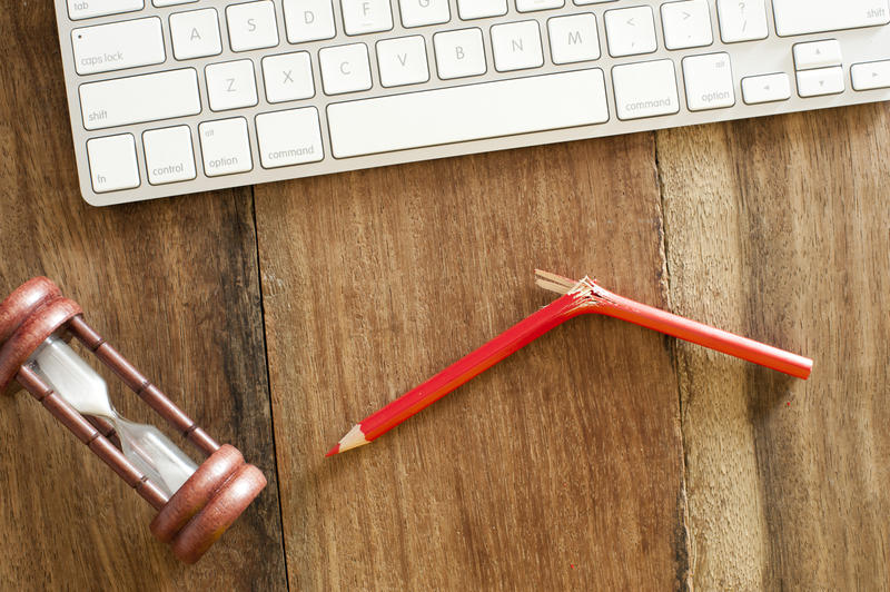 Pressure at work concept with an overhead view of a computer keyboard, egg timer and wooden pencil snapped in half lying on a desk