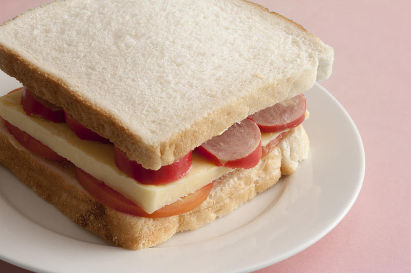 Tasty sandwich using plain white bread with cheese and sausage bits atop sliced tomatos