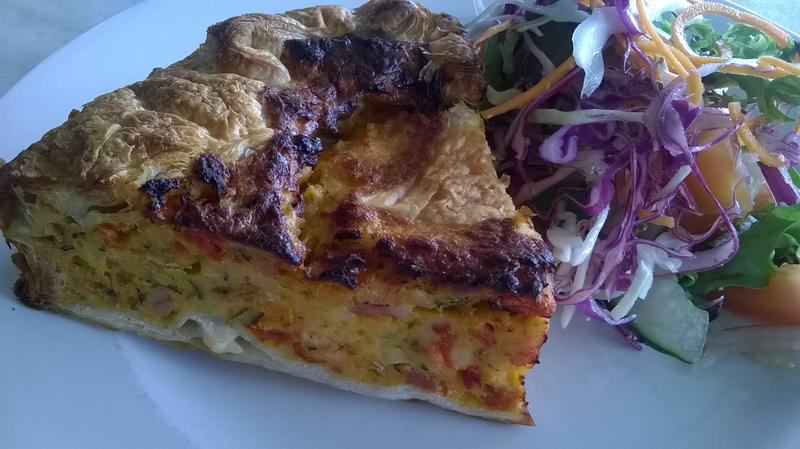 Close up of blackened triangle of quiche beside colorful garden salad on round white plate