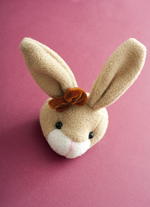 Head of a cute long eared soft plush toy Easter bunny on red with copy space for your holiday greeting viewed high angle