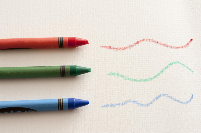 Red, blue and green wax crayons with wavy hand drawn lines in an overhead view on white