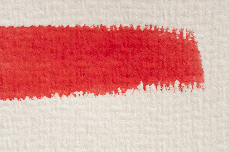 Close up detail of a single red watercolor paint brushstroke on textured paper or canvas with copy space below