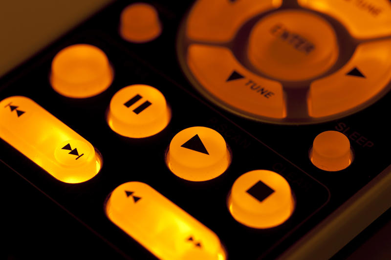 Remote control playback buttons illuminated from inside with warm yellow light in the dark, close-up cropped image