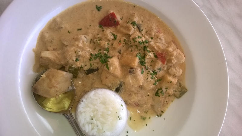 Overhead view of round white plate on rustic table filled with creamy meat dish and steamed rice by spoon