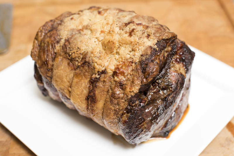 Roast joint of beef fresh from the oven placed on a white square ceramic plate ready to be carved for dinner in a close up high angle view