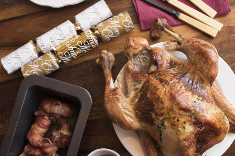 Roast Christmas turkey with bacon rolls or Pigs in Blankets served on a decorated table with Xmas decorations and carving utensils viewed from overhead