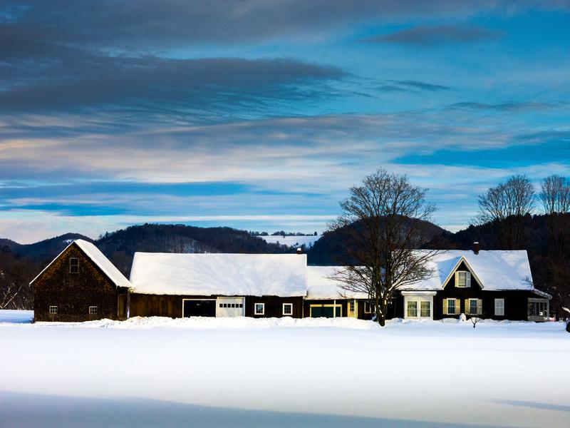 <p>House and barn in Winter at dusk with blue-grey sky, white shadowed snow and shadows on the roof in rural Vermont Woodstock.</p>
