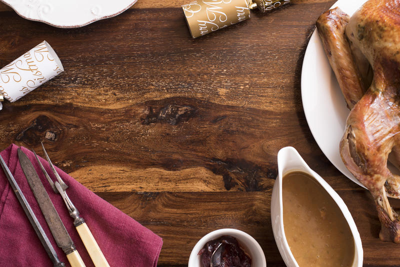 Rustic Christmas dinner table frame and copy space with roast turkey, gravy, utensils, crackers and cranberry sauce in a top down view