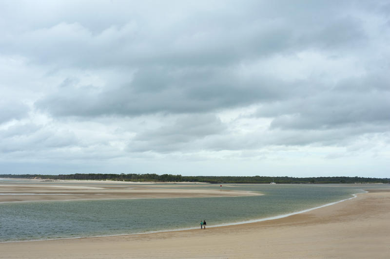 Sandy river mouth forming an estuary as it winds its way out to sea in a flat landscape with people walking along the shore