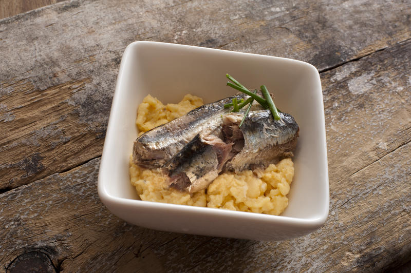 Square white bowl filled with scrambled eggs and raw sardine topped with herbs on rustic wooden table