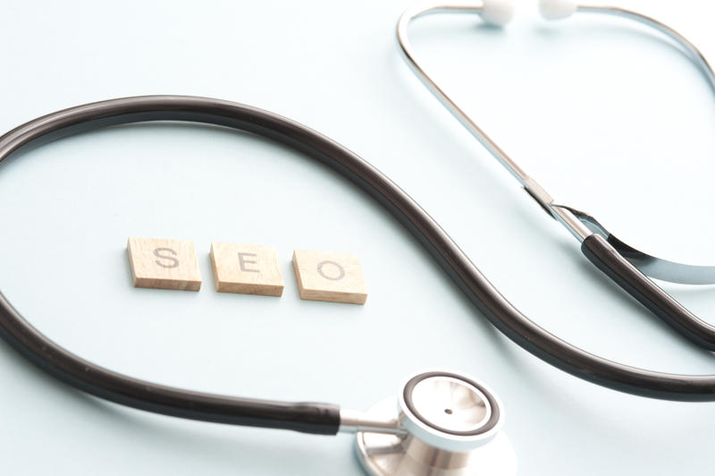 Search engine optimization concept with medical stethoscope and little wooden block letters with the letters S,E and O on light blue background