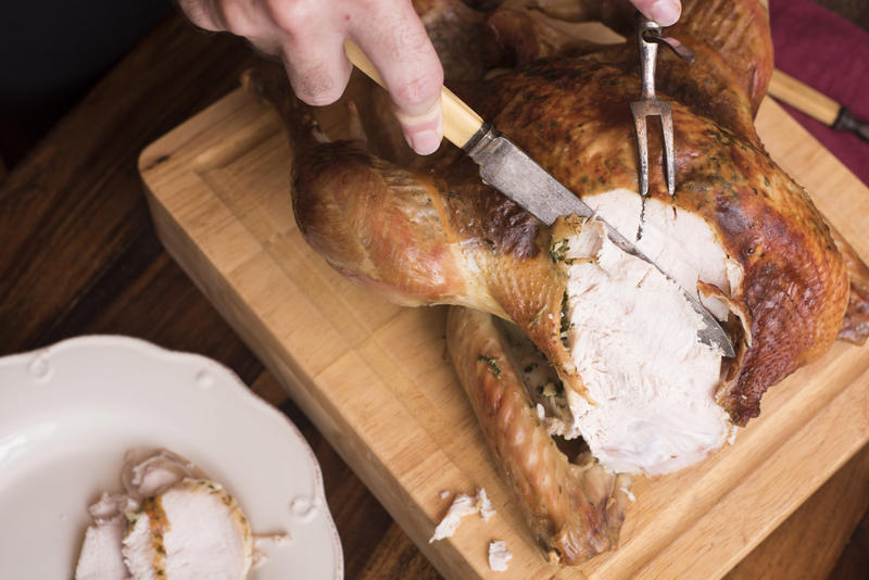 Man slicing a roasted Christmas turkey with vintage bone-handled utensils and placing it onto plates for serving