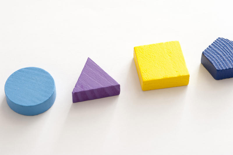 Four basic colorful wooden shapes showing a circle, triangle, square and pentagon in a line on white for educating young children, with copy space