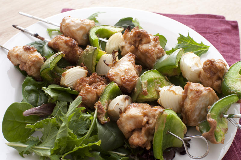 High Angle Still Life of Grilled Kebabs on Bed of Fresh Green Salad Served on White Plate