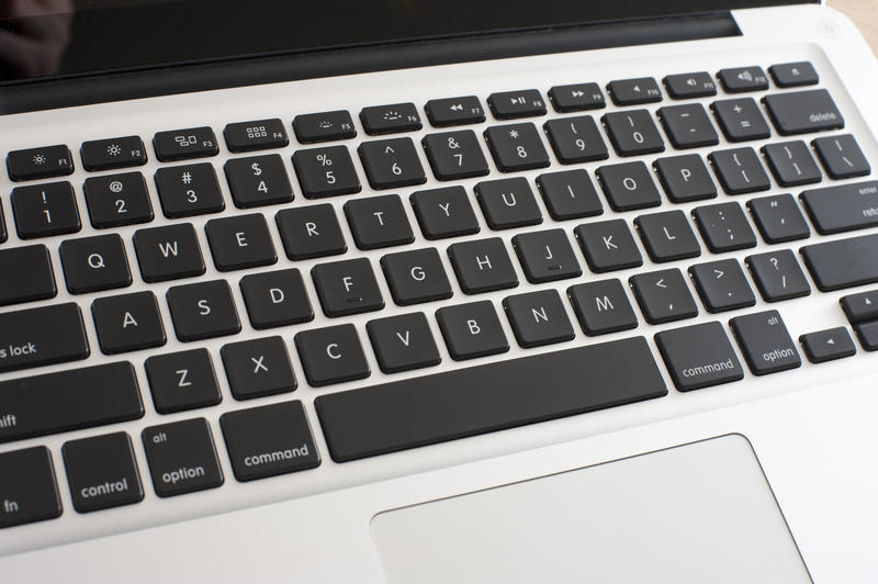 High angle close up view of an open silver laptop showing the touch pad and keyboard with black keys