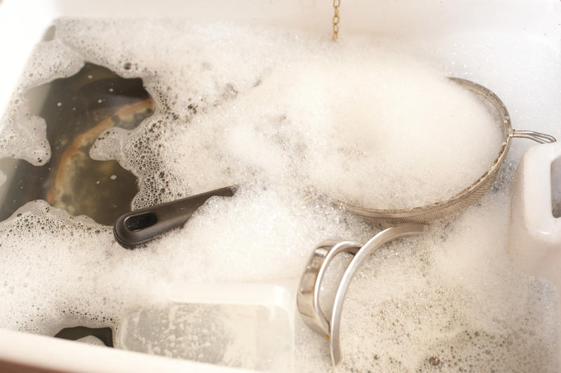 Dirty dishes in soapy water in a sink waiting to be washed after cooking or baking with metal pots and saucepans