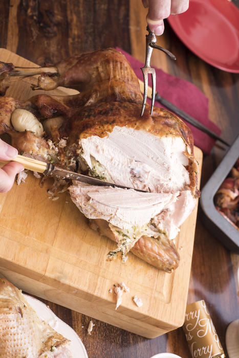 Man carving the white breast meat of a roast turkey into slices on a wooden board on the Christmas or Thanksgiving table
