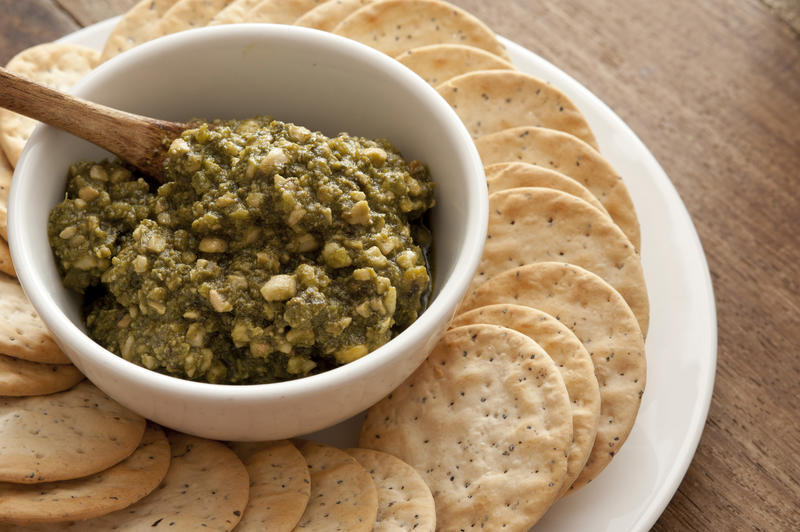 Tasty basil pesto savory dip with water crackers served on a plate on a wooden counter form appetizers or finger food