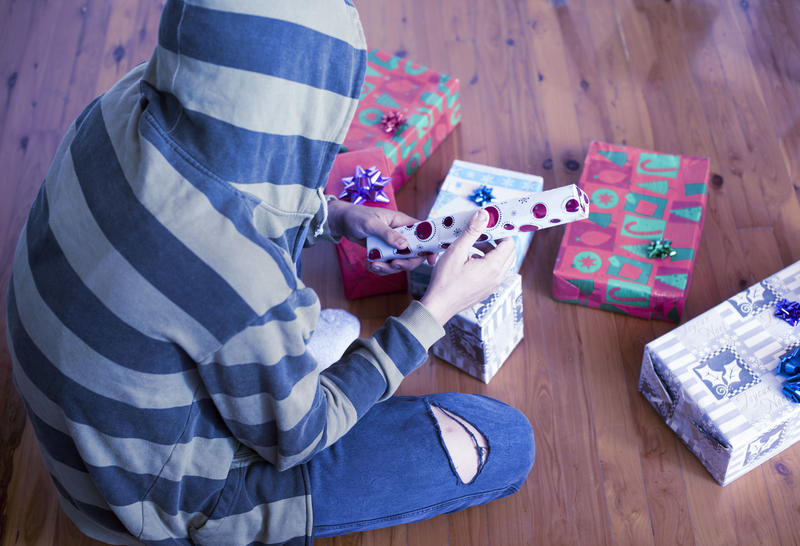 Person wearing a hooded top sitting on the floor opening Christmas gifts on Xmas morning viewed high angle