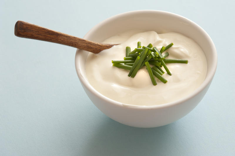 Side dish of sour cream and fresh chopped green chives with a small wooden spoon to accompany a meal as a topping or garnish