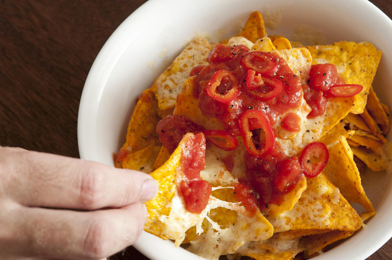 Fingers from hand pulling out tortilla chip coated in melted cheese and cherry salsa