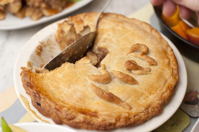 Man eating a pie with a spoon cutting into the delicious pastry crust in a close up view of the pie and utensil