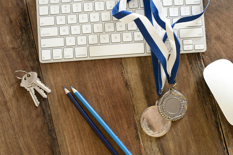 Online sports award concept with two sporting medals lying across a computer keyboard on a wooden desk, high angle view