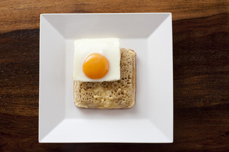 Fun squared shape theme for breakfast with a square fried egg on a square crumpet served on a modern square white plate viewed from above
