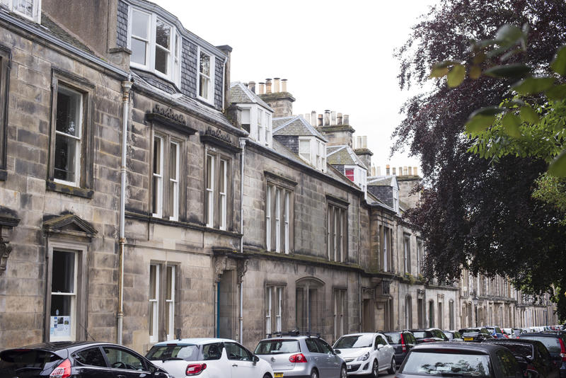 Rows of parked modern cars in front of old traditional stone block homes in Saint Andrews, Scotland