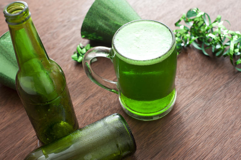 Wooden table covered with party objects, empty bottles and glass mug full of green colored beer for saint patricks day celebrations