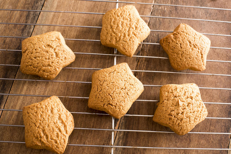 Freshly baked star shaped Christmas gingerbread cookies cooling on a wire rack on a wooden kitchen table viewed from above