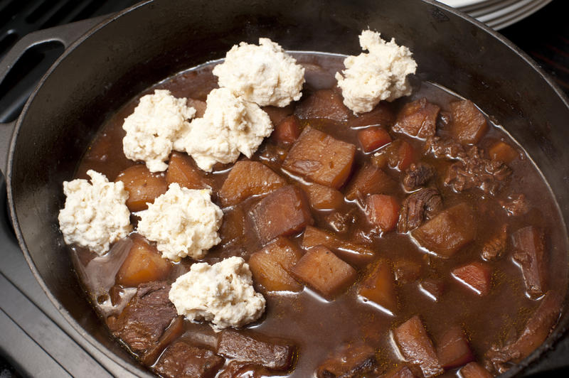 Thick stew with beef chunks and vegetables in broth with uncooked dumplings on top