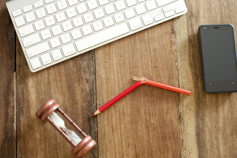 Stress at the office concept with an overhead view of a snapped wooden pencil with an egg timer, mobile and computer keyboard