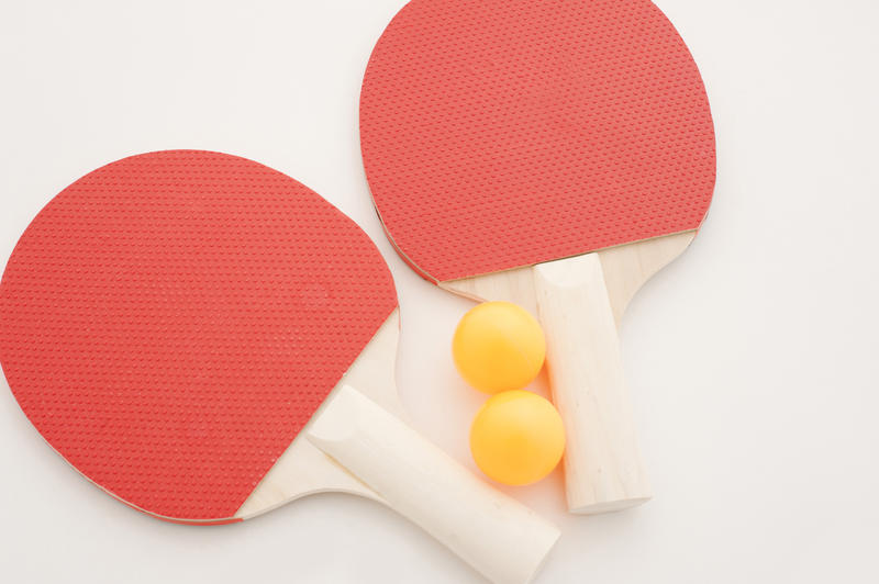 Set of table tennis equipment with two red wooden ping pong bats and two yellow balls on a white background, overhead view with copy space