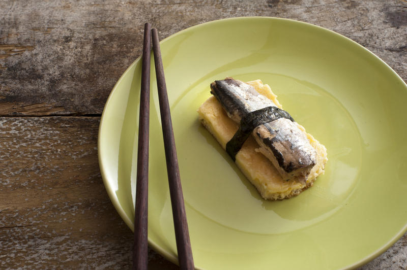 Piece of tamagoyaki and fish pieces prepared with salt and bound together at center of green plate with brown chopsticks over wooden table