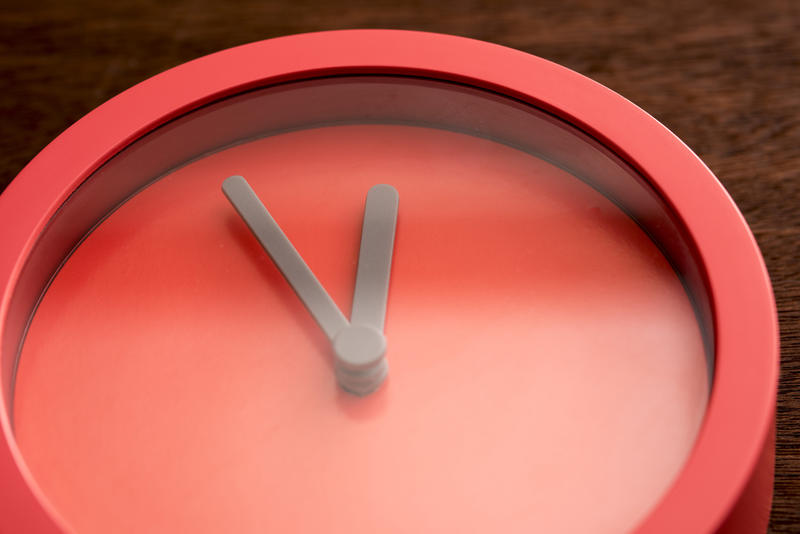 Blank face clock made from red plastic with hands on the time of eleven fifty five. Includes copy space.