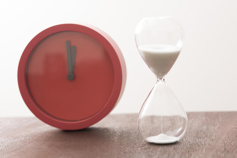 Modern red timer clock with an egg timer with running sand standing side by side on a kitchen counter counting down the passing time
