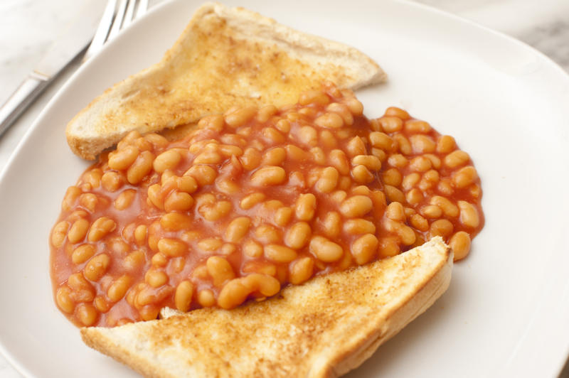 Sweet and savory baked beans in tomato sauce and with buttered toast placed on either side on a white plate beside utensils