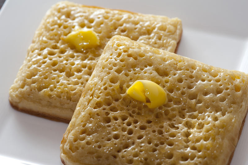 Close up of butter melting on two crumpets shaped like a square on a white plate