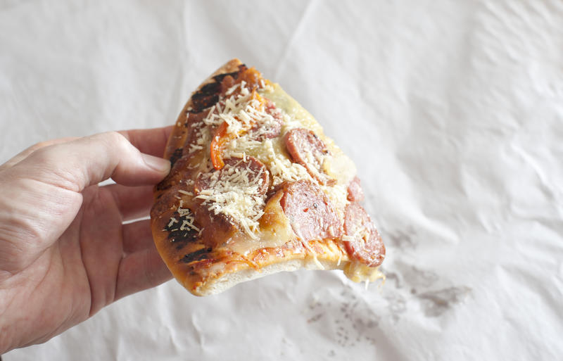 Man holding the last slice of salami or pepperoni pizza topped with spicy sausage, cheese and onion over crumpled white paper