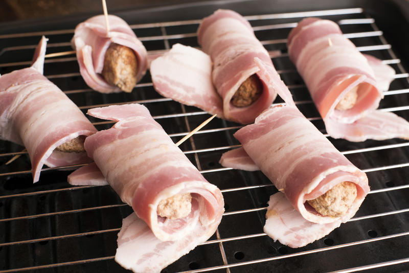 Uncooked Pigs in Blankets or Bacon Rolls with rashers of bacon wrapped around pork sausages ready for cooking on a grill pan