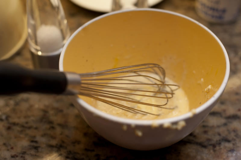 Dirty mixing bowl with a metal hand whisk and the remnants of a baking mixture on a marble kitchen counter, high angle view