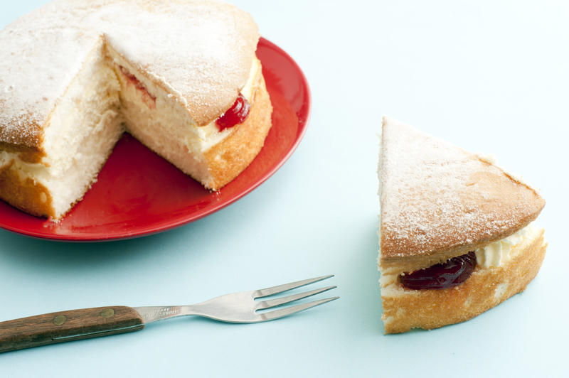 Single small size victoria sponge cake dessert with cut out piece and fork on light blue table