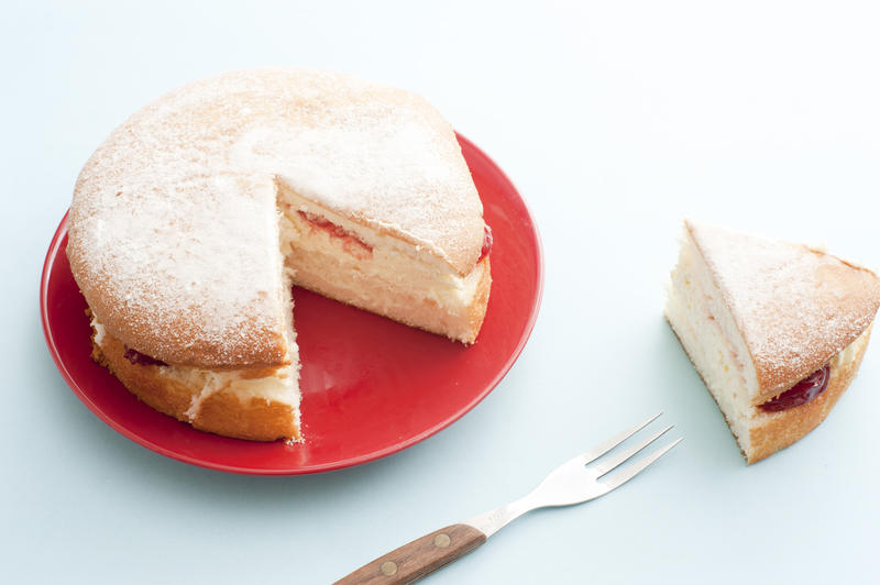 Tasty freshly baked Victoria sponge cake filled with whipped cream and strawberry jam and topped with sprinkled icing sugar with one slice removed to the side