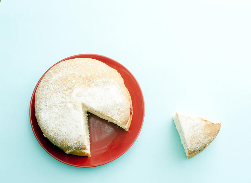Homemade Victoria sponge cake with a cut slice set to the side, overhead view on a red plate on a blue background with copy space