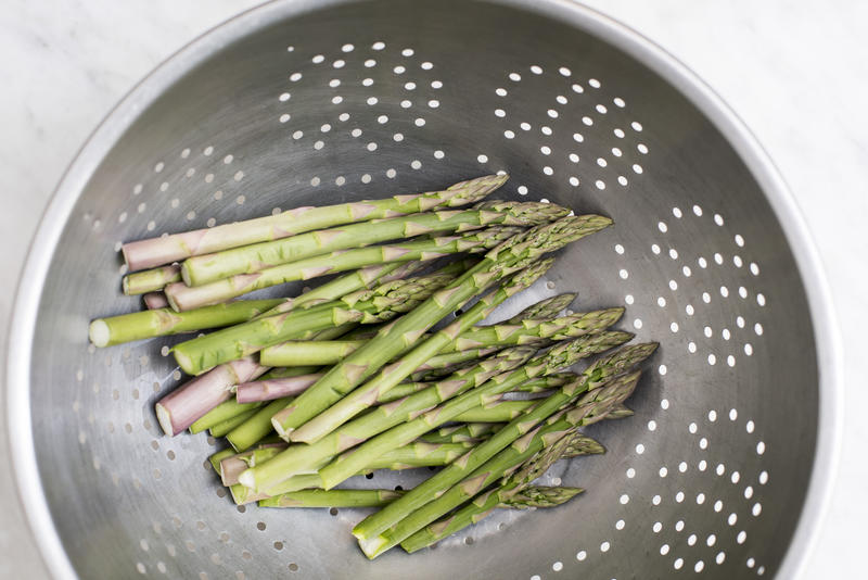Washing healthy fresh green asparagus spears in a metal colander viewed from above