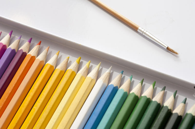 Cropped view of sharp purple, orange, blue and green hue colored pencils in box next to small paintbrush