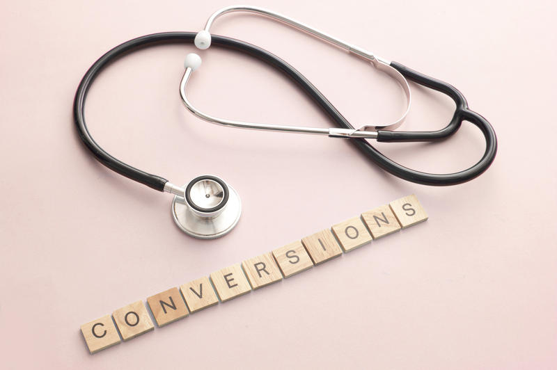 Website marketing concept with medical stethoscope and little wooden block letters with letters spelling out conversions over pink background