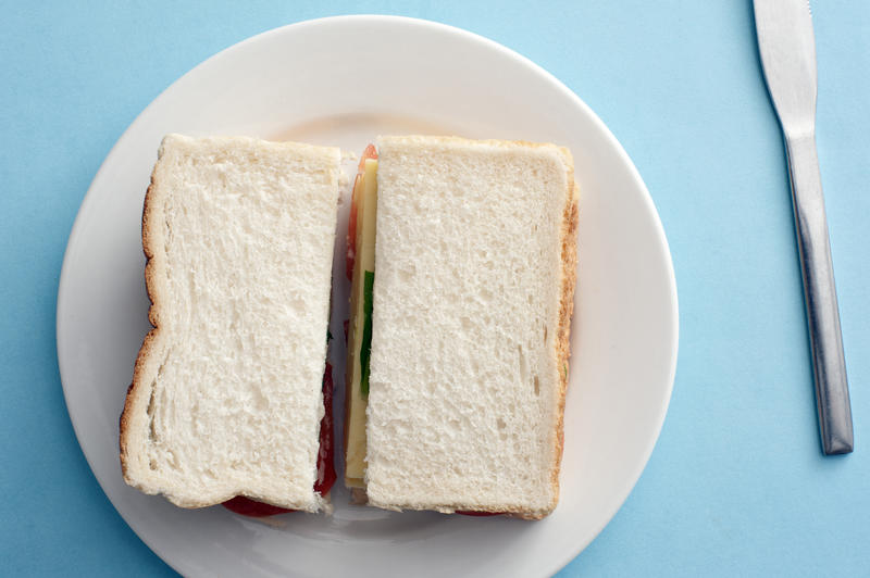 Above view on white bread sandwich in round plate with table knife beside it over blue background