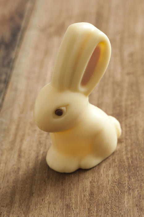 Close up view of white chocolate easter bunny sitting on wooden table surface background